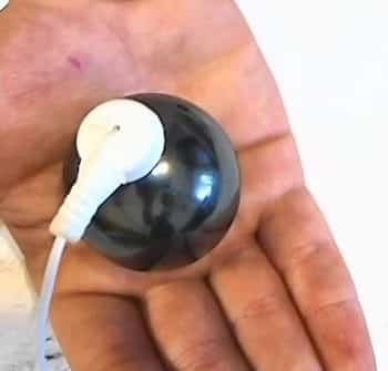Hand holding a black Shungite sphere electrode connected to a white cable adapter.