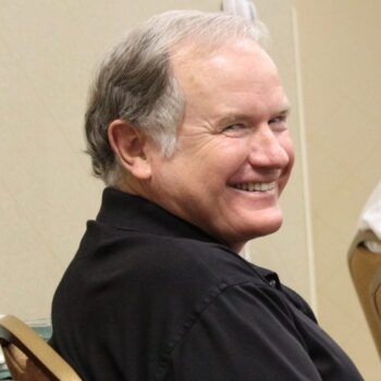 Mike Beasley smiling and looking over his shoulder while wearing a black polo shirt.
